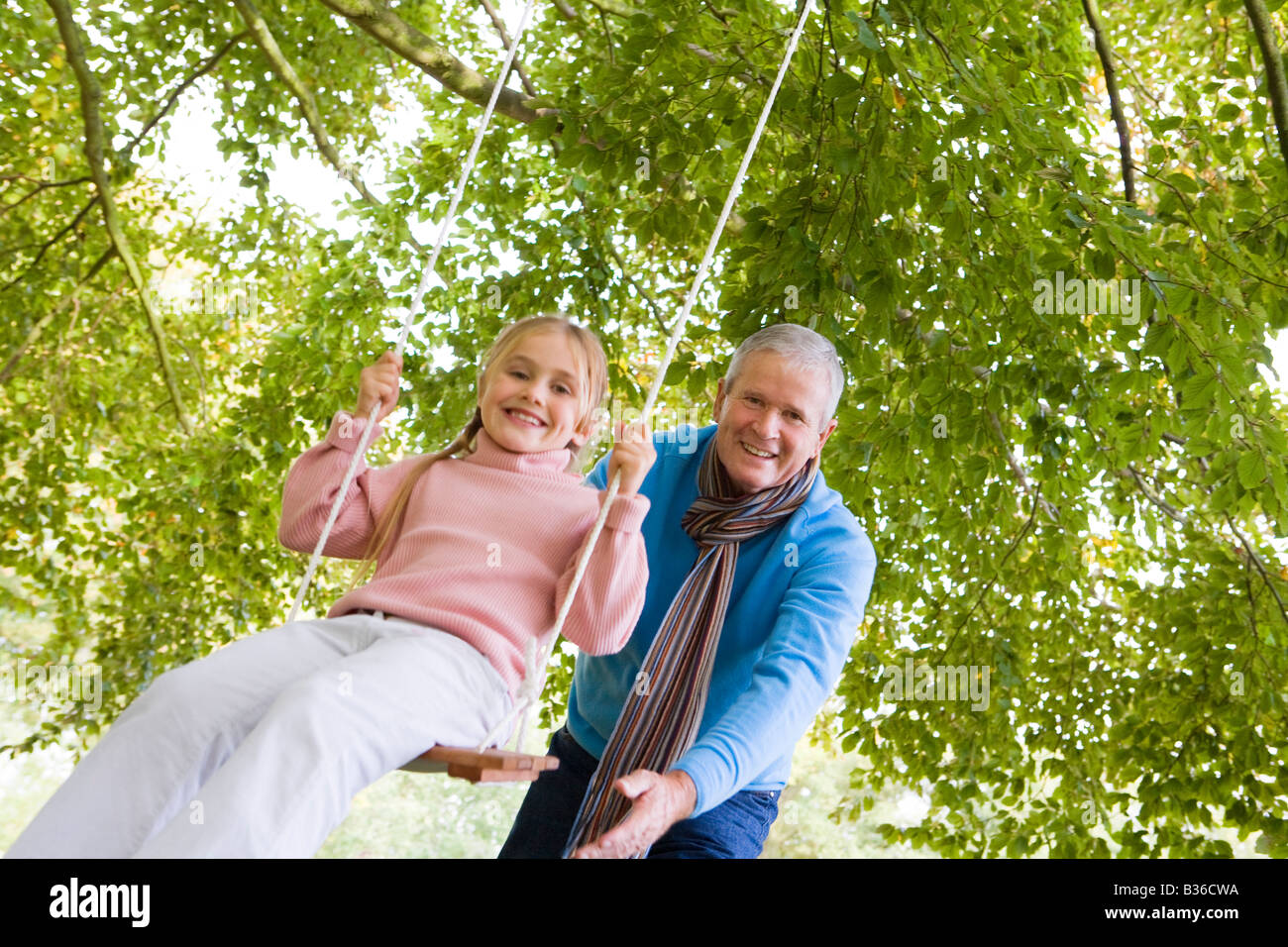 Nonno all'aperto spingendo la nipote dello swing e sorridente (messa a fuoco selettiva) Foto Stock