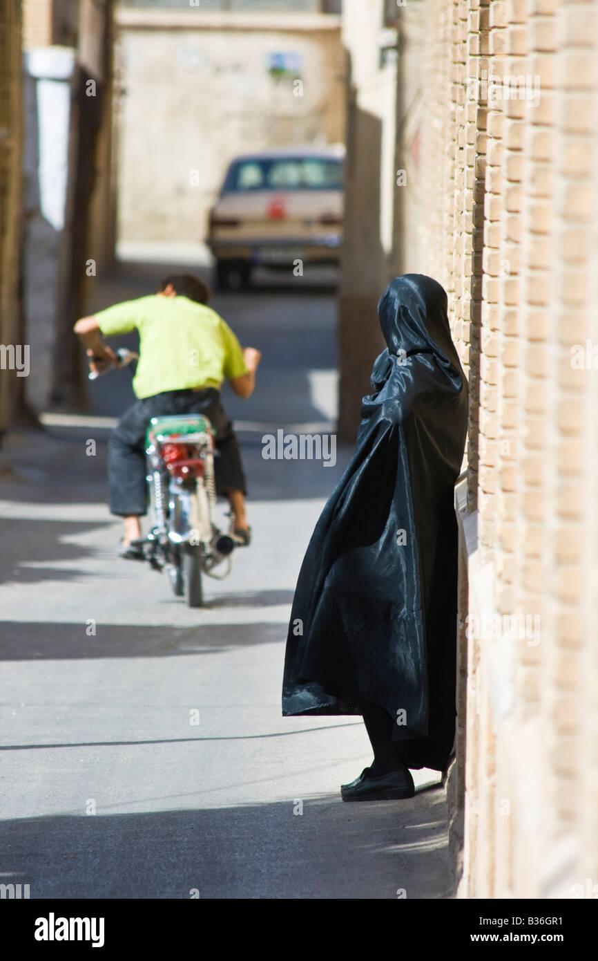 Donna che indossa un chador a guardare una moto passano per le strade di Shiraz Iran Foto Stock