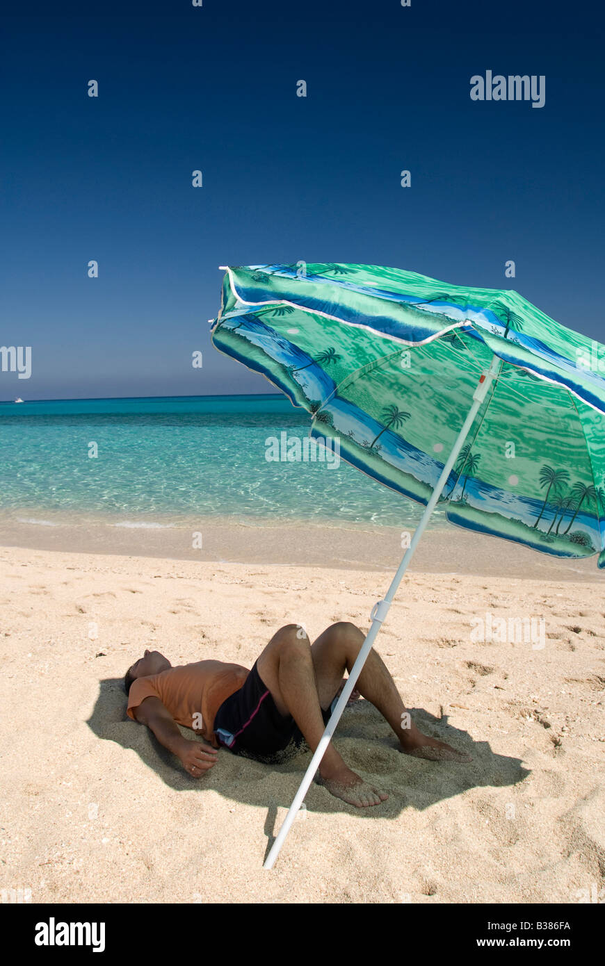 Un uomo rilassante sotto ombrellone in spiaggia Foto Stock