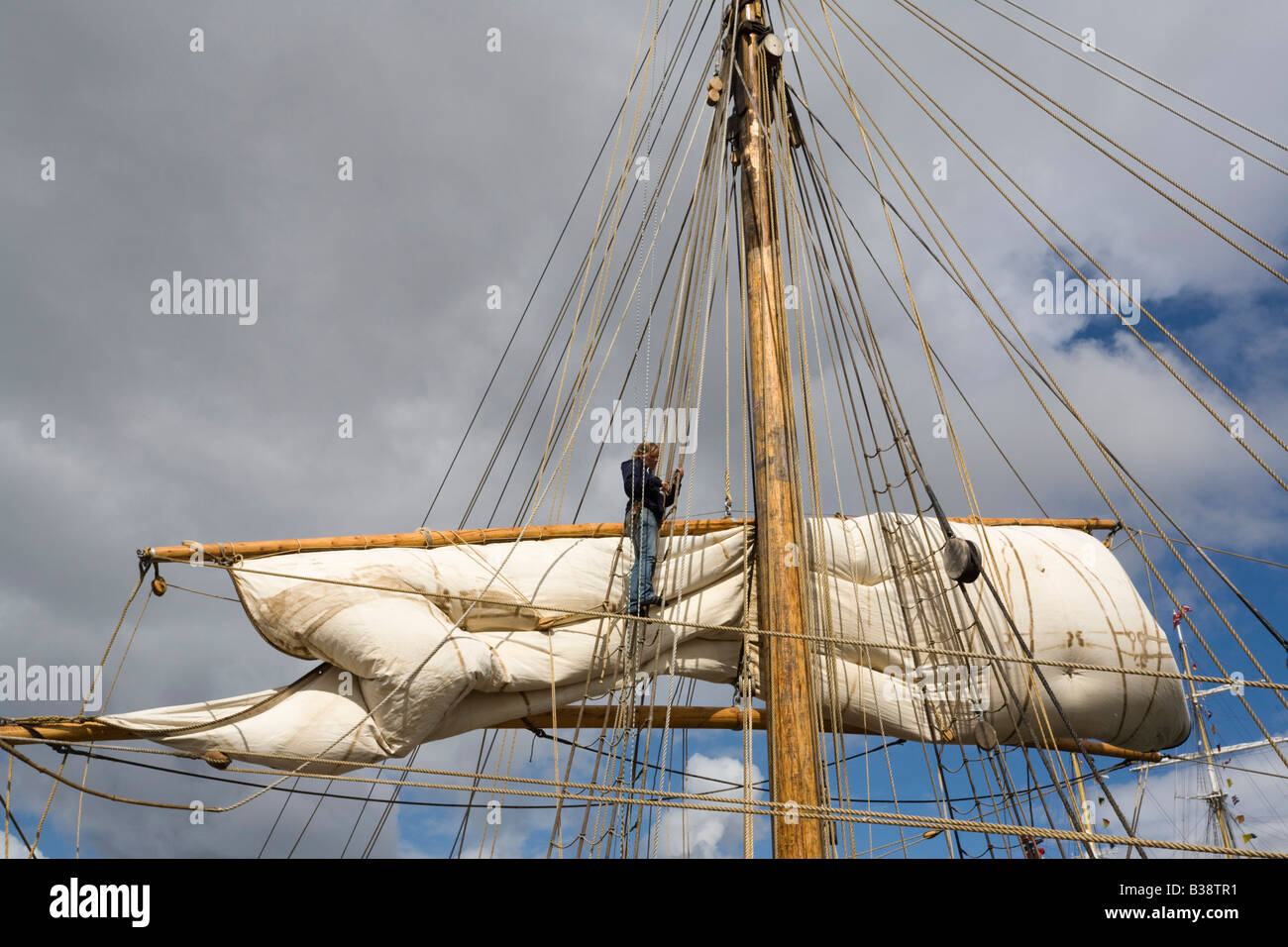 Persona le funi di smistamento e la vela in alto sulla piazza montante truccate sulla barca in Tall Ships race sailor lavorando Foto Stock