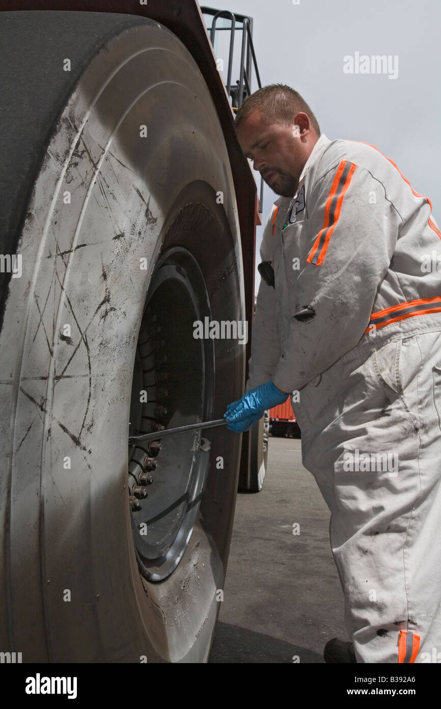 Un lavoratore di manutenzione sostituisce un pneumatico su attrezzature utilizzati per spostare i contenitori di spedizione nel porto di Oakland Foto Stock