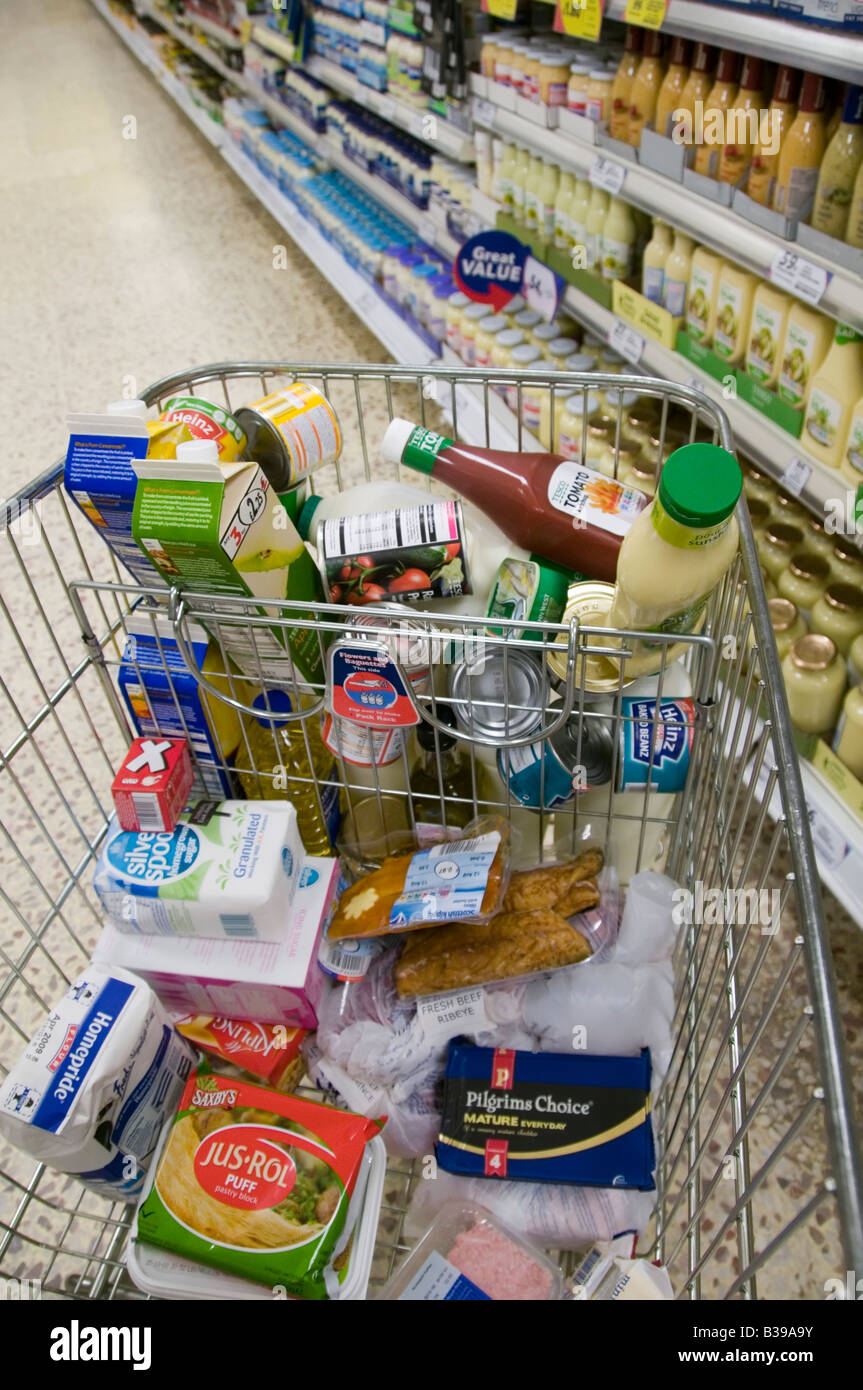 Tesco Supermarket carrello carrello per lo shopping di cibo in Aisle accanto scaffali della drogheria Inghilterra UK Foto Stock