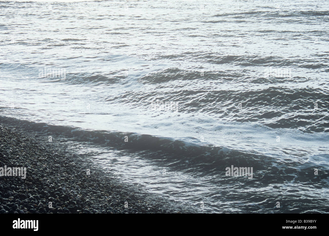 Un invitante colore grigio argento mare con grande rottura rigonfiamento sulla riva di punta arrotondata ciottoli grigio Foto Stock