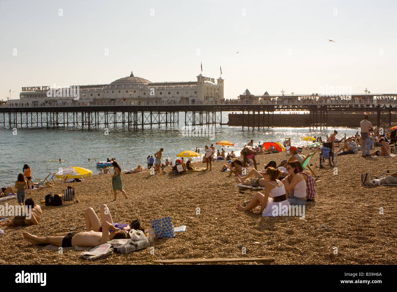 La gente a prendere il sole sulla spiaggia di Brighton Pier in background Foto Stock