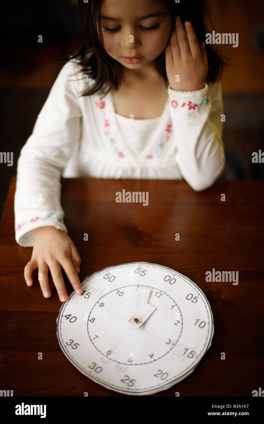 Bambina di cinque anni racconta il tempo con un orologio di carta il suo fratello più anziano realizzato a scuola Foto Stock