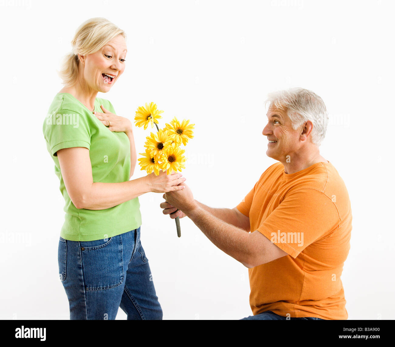 Uomo di mezza età in ginocchio dando donna bouquet di fiori gialli Foto Stock