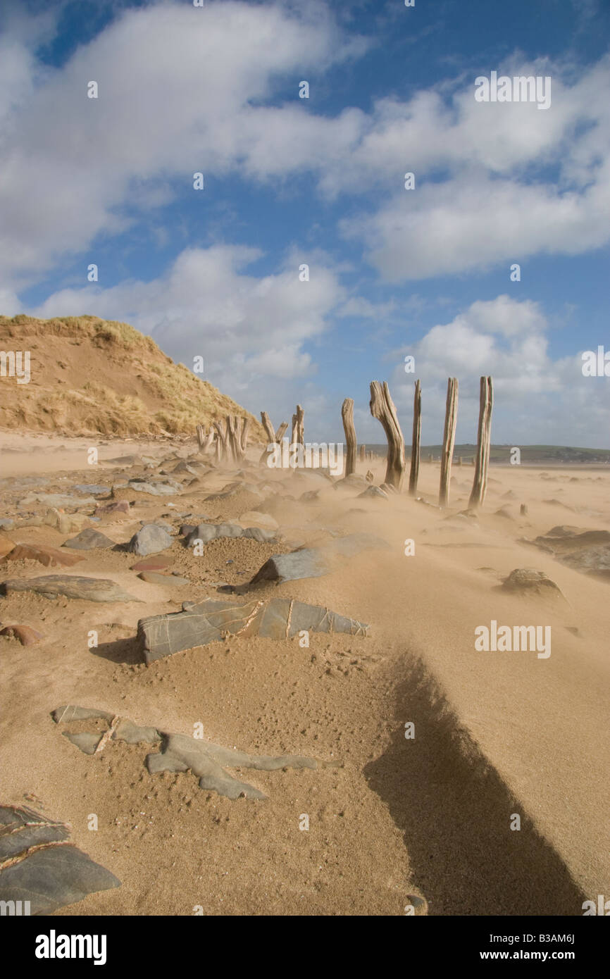 Ventoso spiaggia con sabbia, massi e abbandonati linea di recinzione che mostra erosione lungo una spiaggia in Devon UK Foto Stock