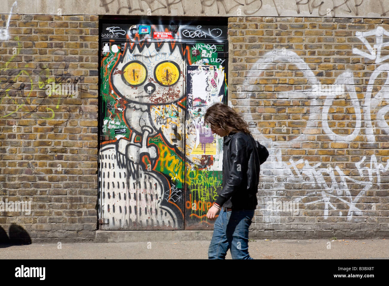 Coperto di graffiti e porta capelli lunghi uomo in giacca di pelle. Hanbury Street, Shoreditch, Londra, Inghilterra Foto Stock
