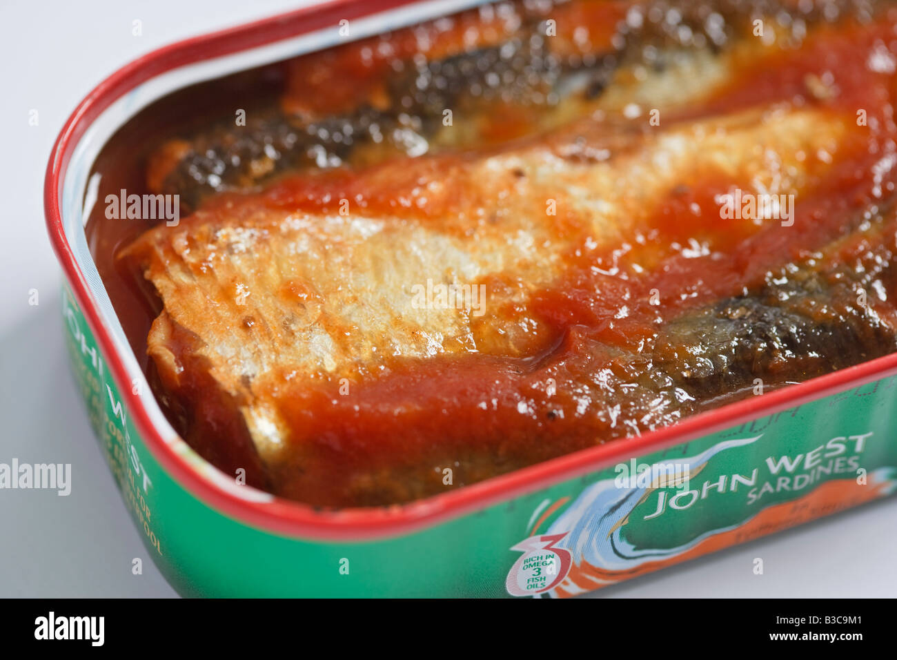 Aprire una scatola di sardine contemplati in salsa di pomodoro contro uno sfondo bianco Foto Stock
