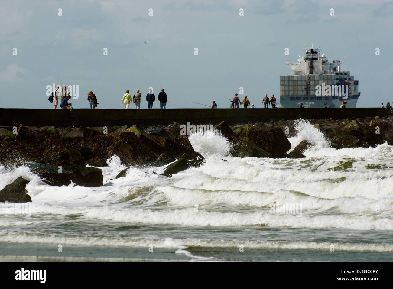Gruppo di persone a piedi levee dyke dam Hoek van Holland spiaggia onde enormi vento alto mare Nave di grandi dimensioni dietro, Paesi Bassi Foto Stock