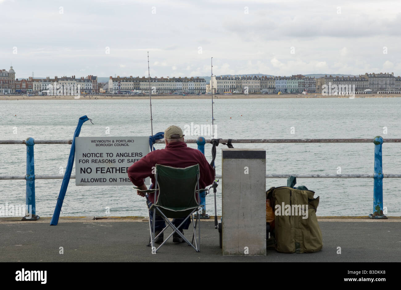 Fisherman rilassante nella sua sedia e godendo la vista del lungomare di Weymouth mentre la pesca sportiva alla fine del braccio del porto Foto Stock