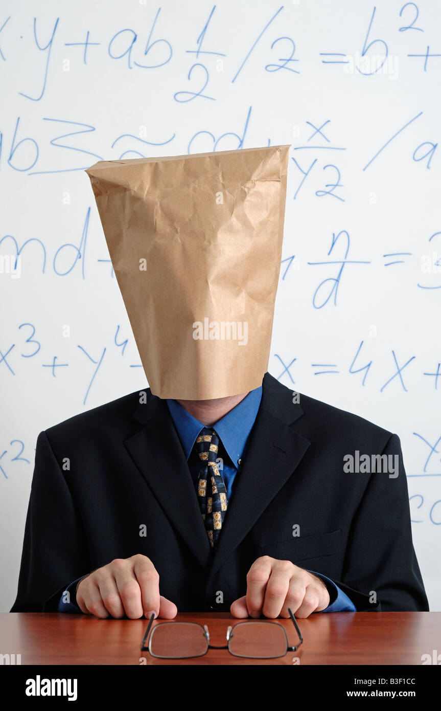 Uomo in un vestito con un sacchetto di carta sulla sua testa seduto dietro la sua scrivania Foto Stock
