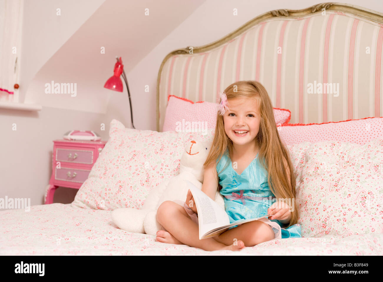 Giovane ragazza seduta sul letto con prenota sorridente Foto Stock