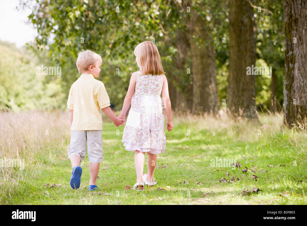 Due giovani figli che camminano sul sentiero tenendo le mani Foto Stock