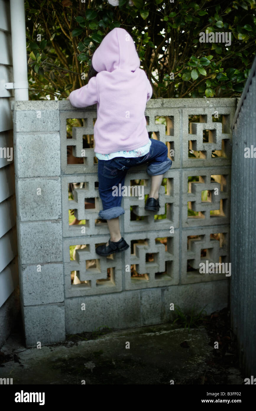 Oltre il Muro bambina di cinque anni arrampica su un basso muro del giardino Foto Stock