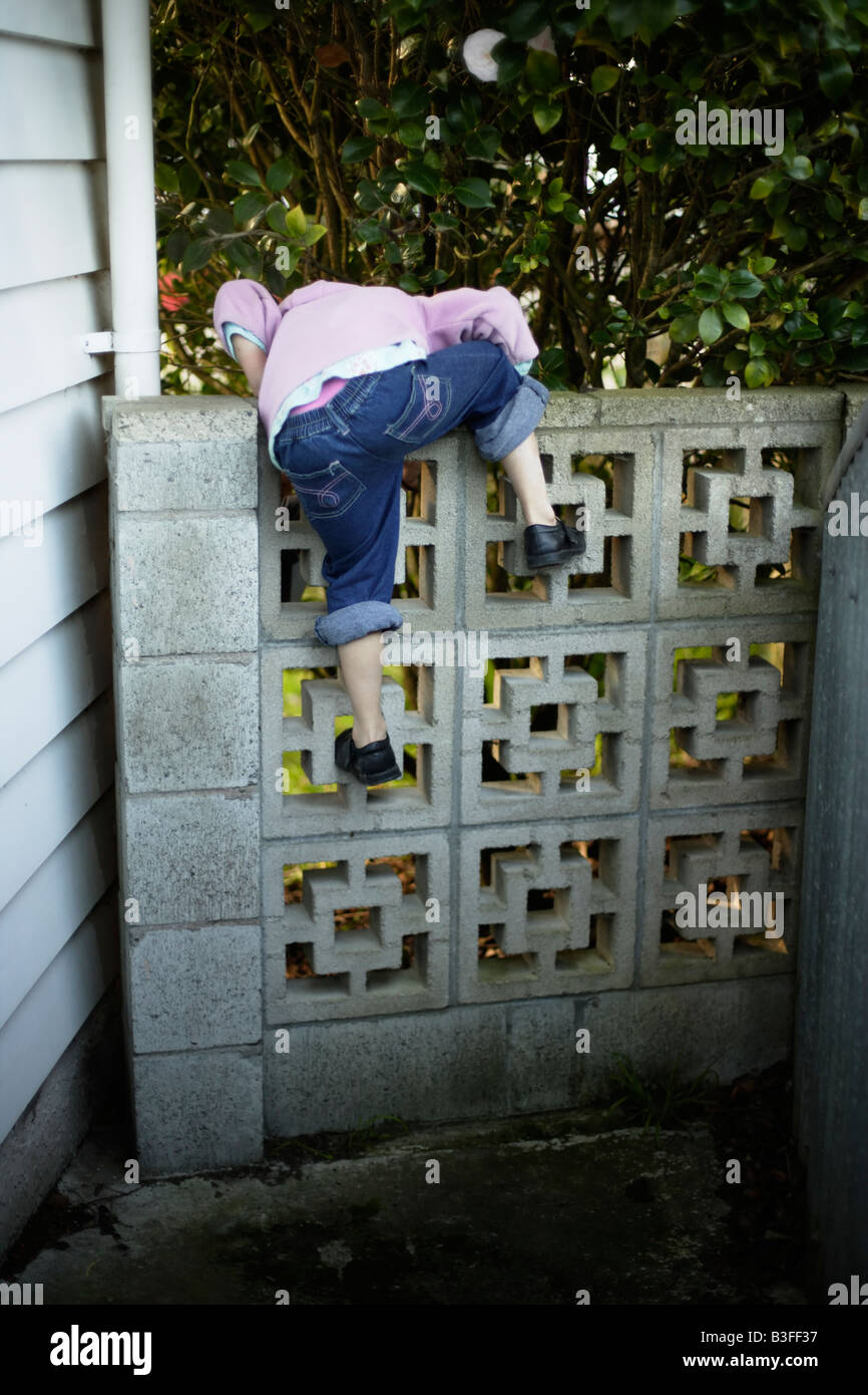 Oltre il Muro bambina di cinque anni arrampica su un basso muro del giardino Foto Stock