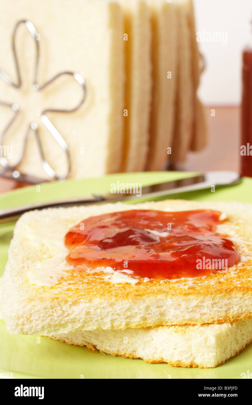 Toast con burro e marmellata di fragola il vasetto di vetro nella piastra bianca con morbida ombra su piazza sullo sfondo del tappeto di profondità del fie Foto Stock