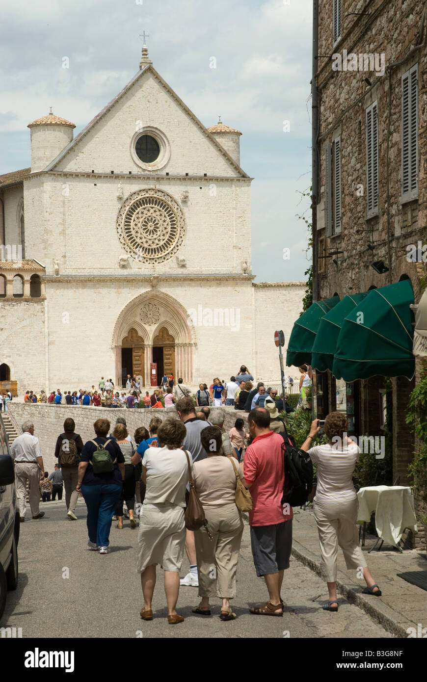 I turisti in folla atBasilica di San Francesco ad Assisi. Il monastero francescano (Sacro Convento) e la parte inferiore e la chiesa superiore (Basilica inferiore e superiore) di San Francesco furono iniziati subito dopo la sua canonizzazione nel 1228. Simone di Pucciarello ha donato la terra per la Chiesa, una collina sul lato ovest di Assisi, noto come 'Collina dell'Inferno" (it. Collo d'Inferno - qui i criminali sono state messe a morte). Oggi, questa collina è appropriatamente chiamato 'Collina del Paradiso". Foto Stock
