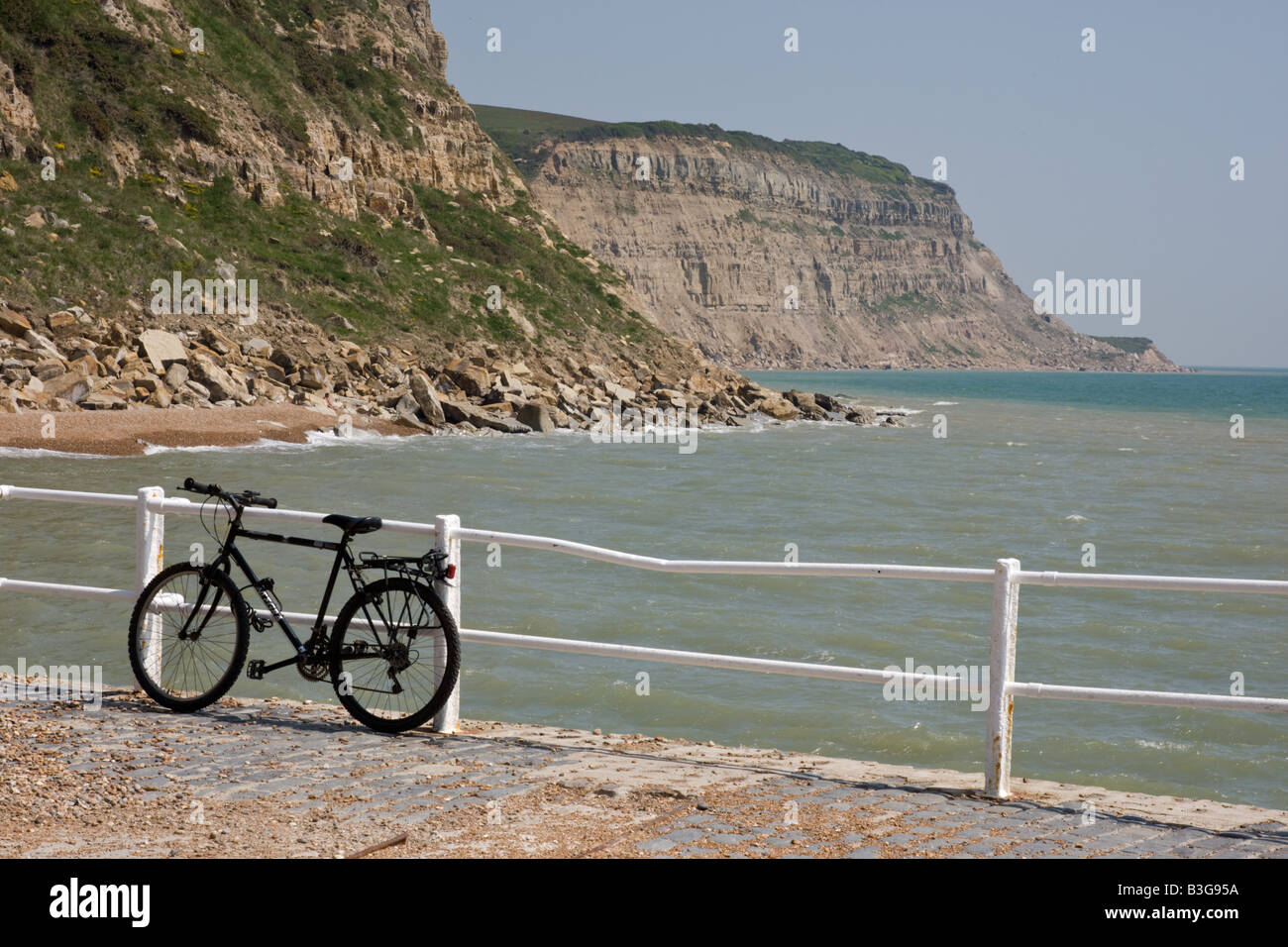 Noleggio siede contro white ringhiere sul lungomare di Hastings con scogliere dietro. Foto Stock