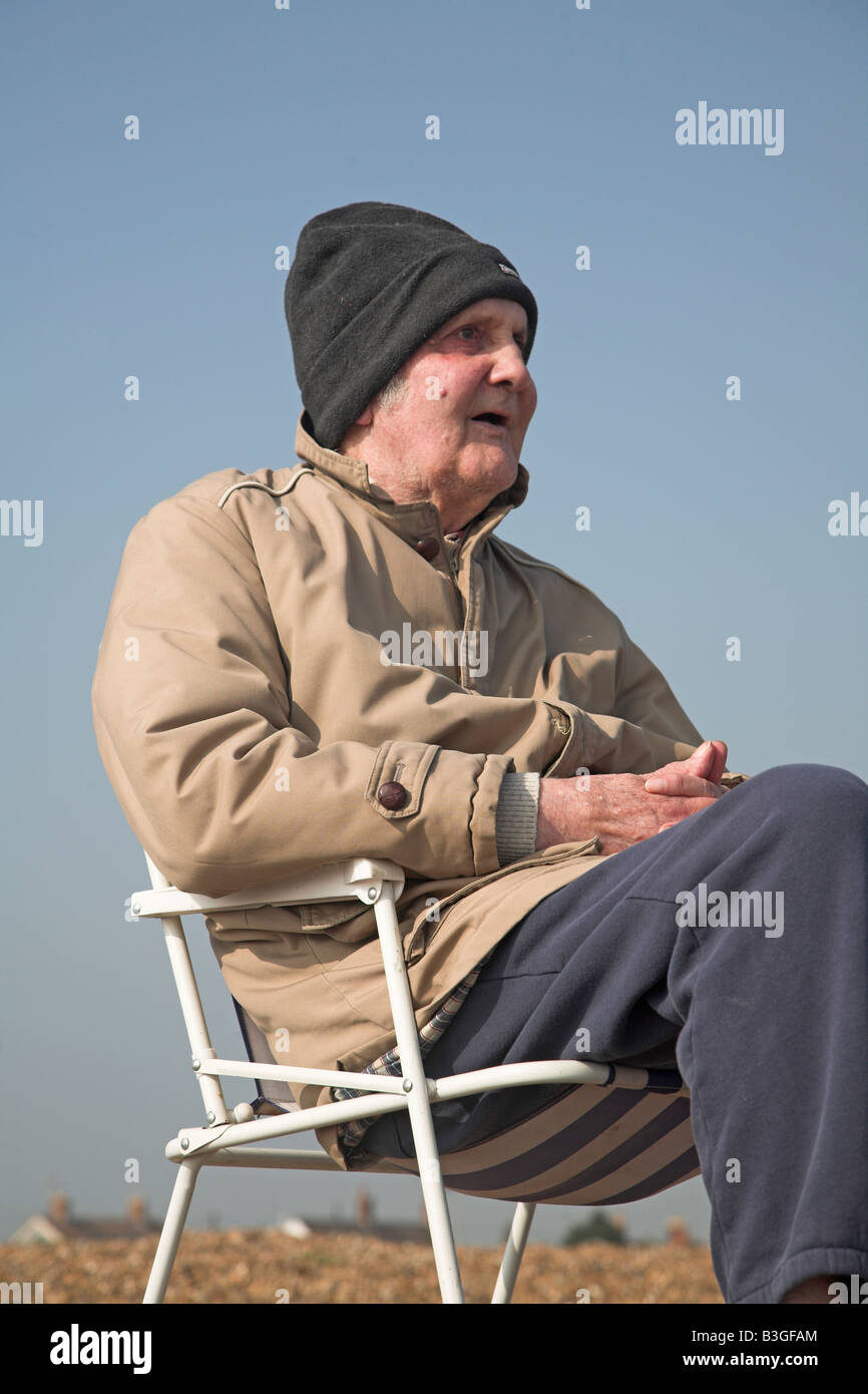 Uomo anziano seduto sulla spiaggia in cattedra Foto Stock