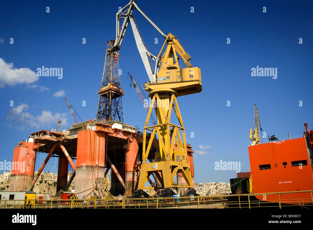 Basso angolo di visione di un impianto di trivellazione petrolifera con una città sullo sfondo, Vallett, Malta Foto Stock