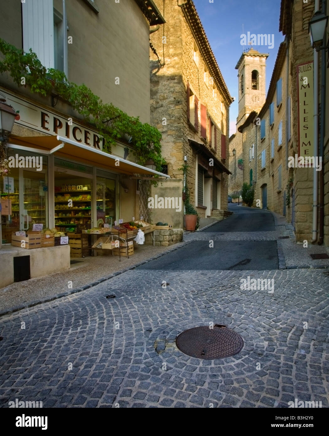 Le strade di ciottoli di Chateauneuf-du-Pape con l'epicerie (un comodo negozio) e il campanile di una chiesa in background Foto Stock