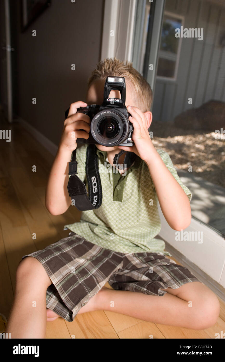 Quattro anni di bambino tiene la fotocamera, seduto sul pavimento a casa Foto Stock