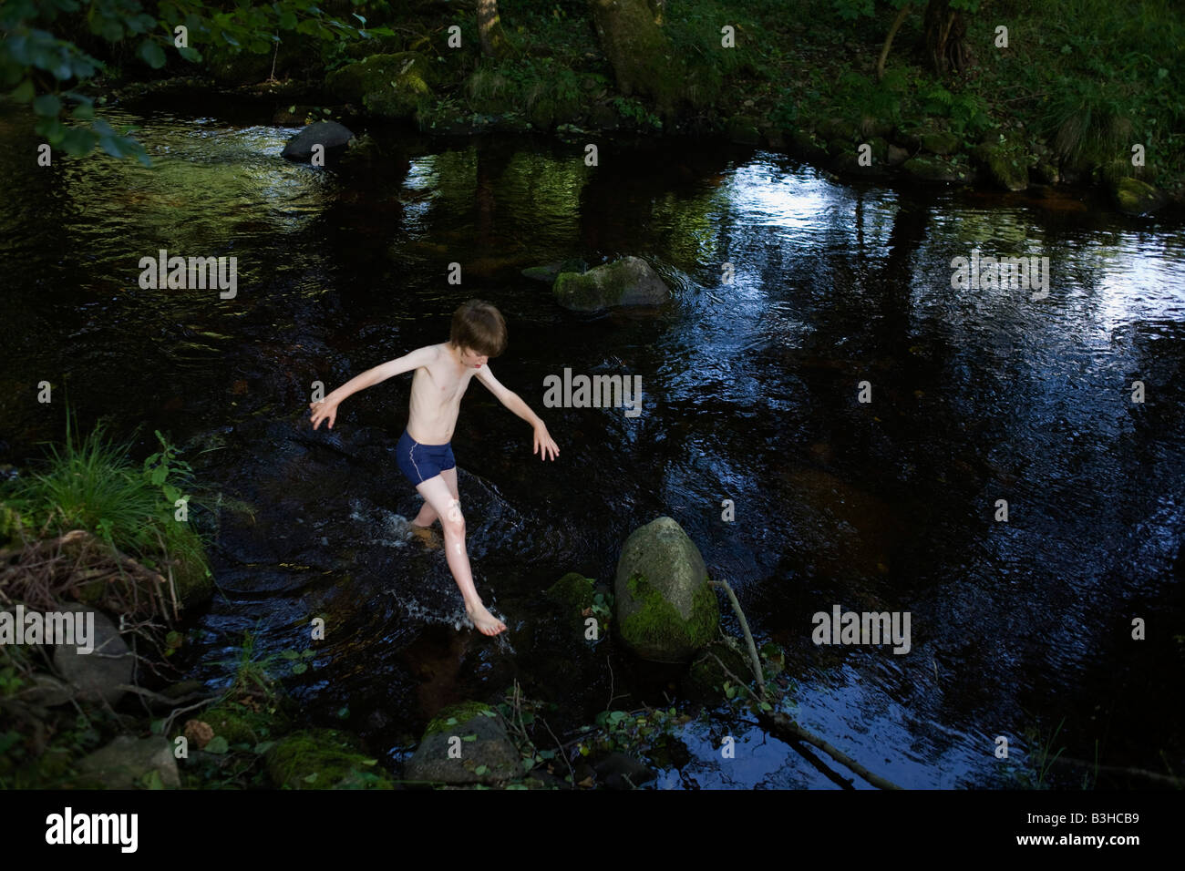 Indossa il suo costume da bagno un giovane avventuriero passeggiate con cautela su rocce scivolose in lordo fiume Enz tedesco Foresta Nera Foto Stock