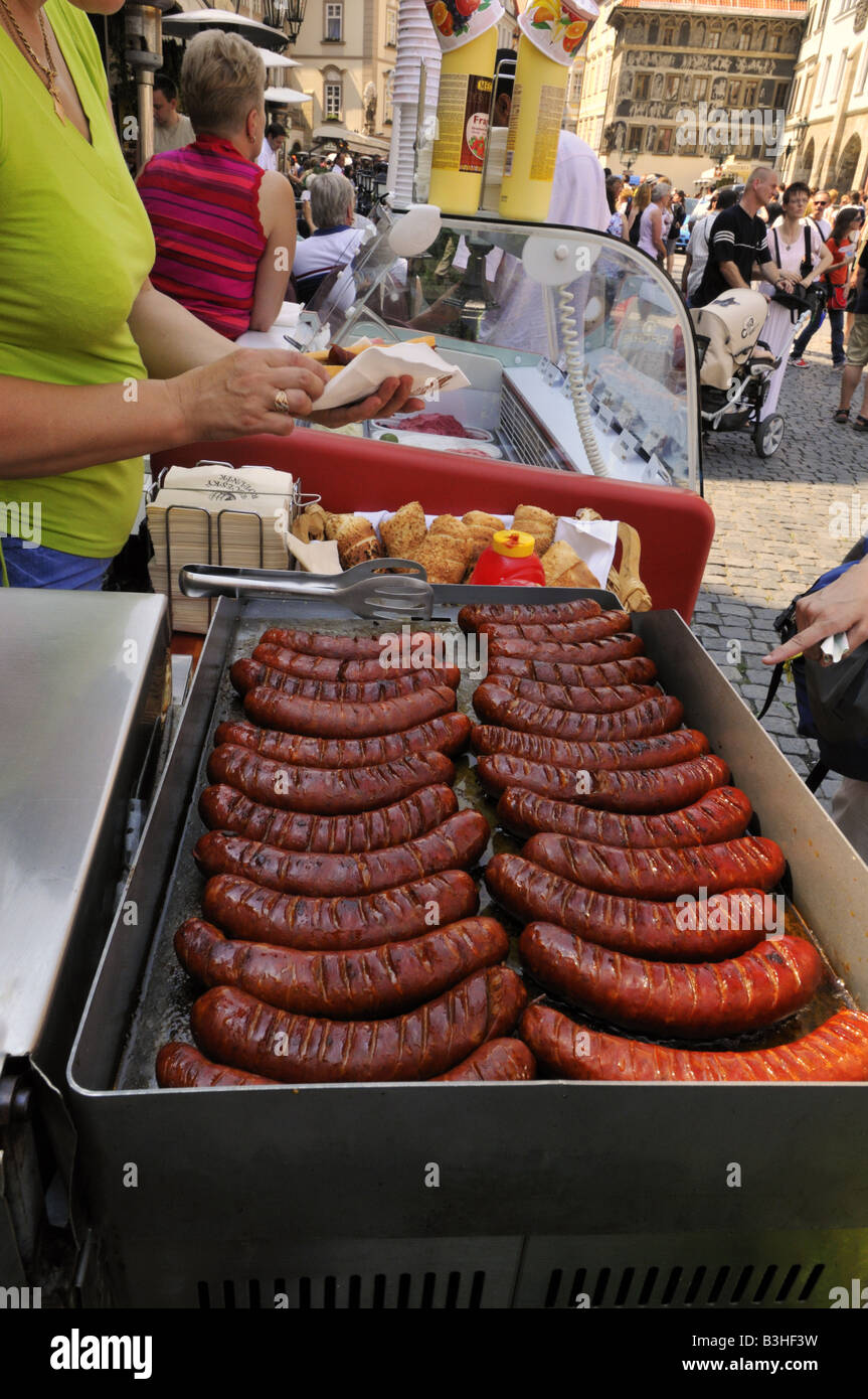 Acquisto di una spessa grasso salsiccia ceca in un rotolo da una donna stallholder in Prague Old Town Square Foto Stock