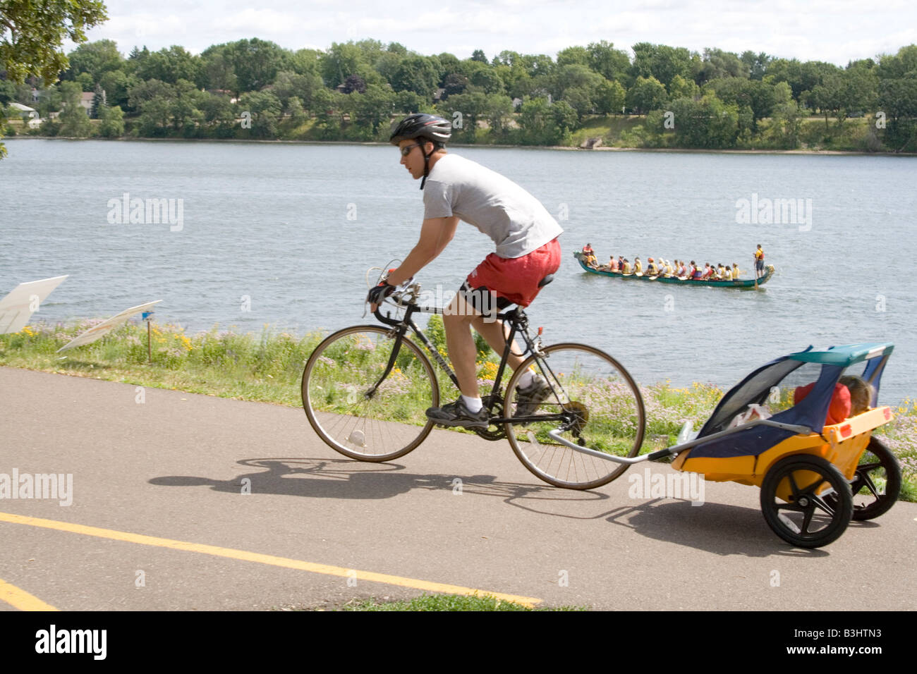 Padre peddling bicicletta con i bambini nel carrello e dragon boat sul lago. Dragon Festival Lago Phalen Park St Paul Minnesota USA Foto Stock