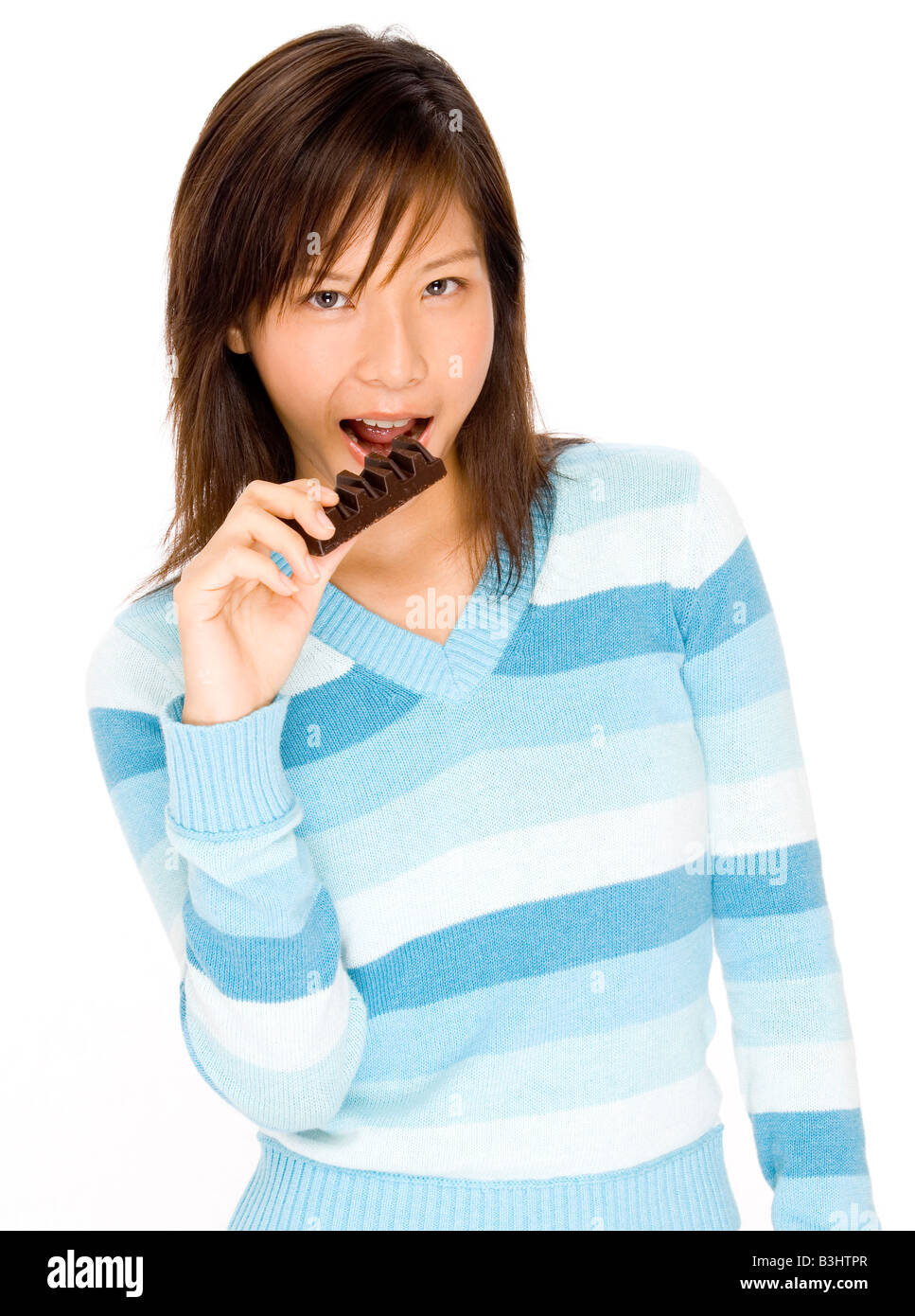 Un simpatico giovane ragazza asiatica di mordere a una barretta di cioccolato Foto Stock