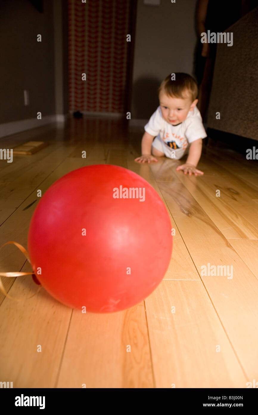 Otto mesi di età bimbo gattona verso il rosso palloncino a home Foto Stock