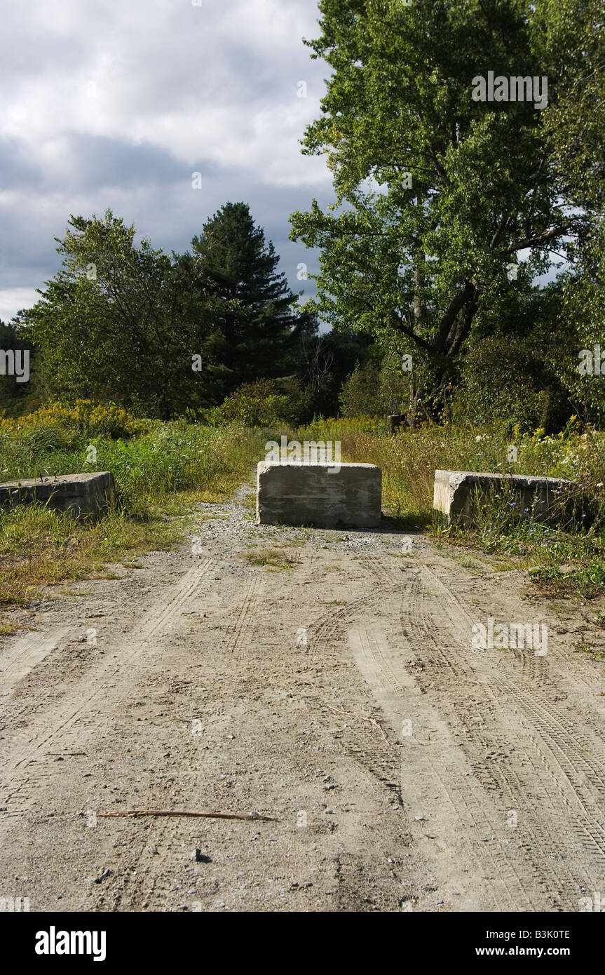 Fine di una strada sterrata bloccato con enormi blocchi di cemento con alberi e cielo molto nuvoloso in background Foto Stock
