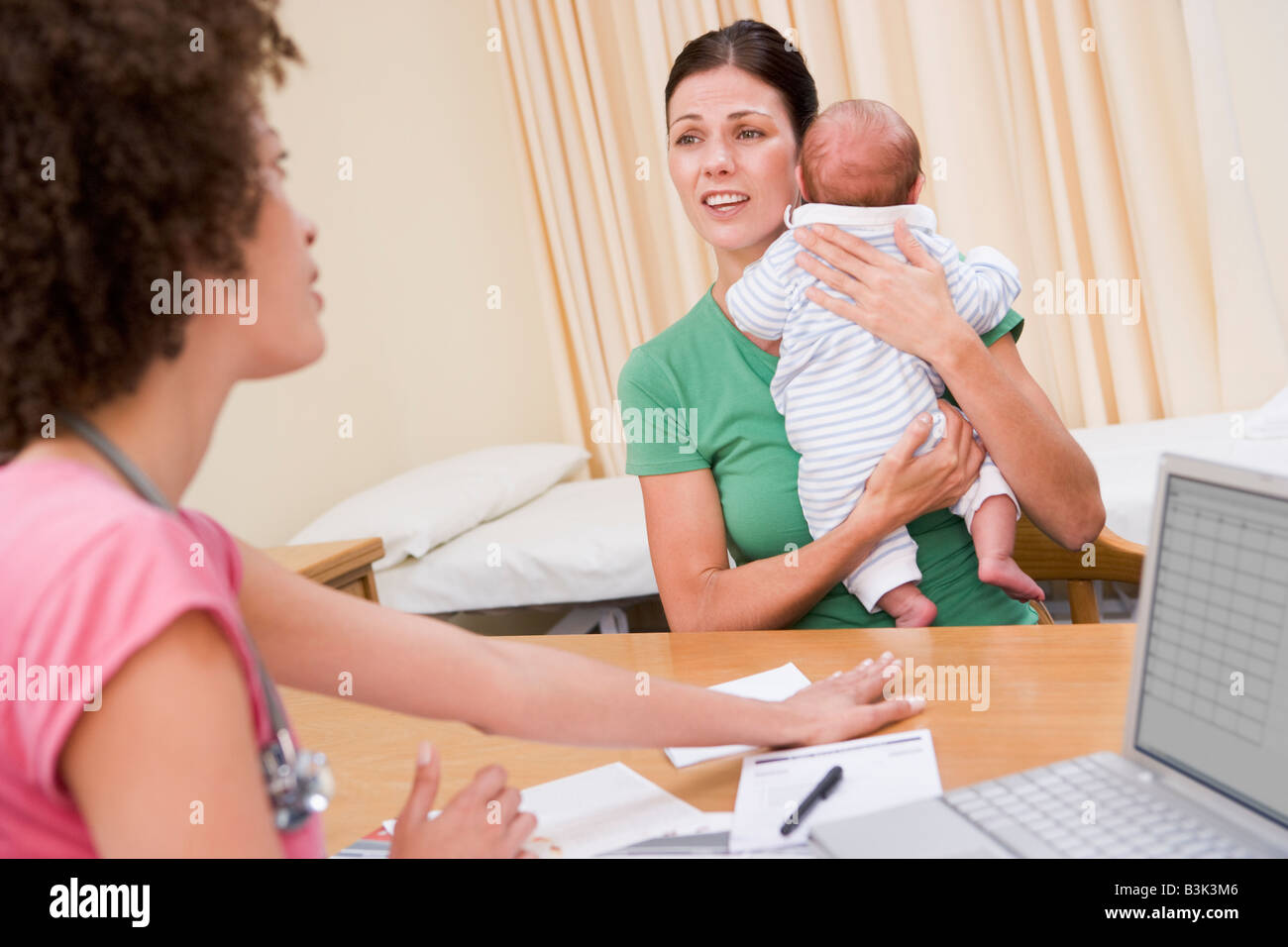 Medico con il computer portatile e di una donna nell'ufficio del medico tenendo baby Foto Stock