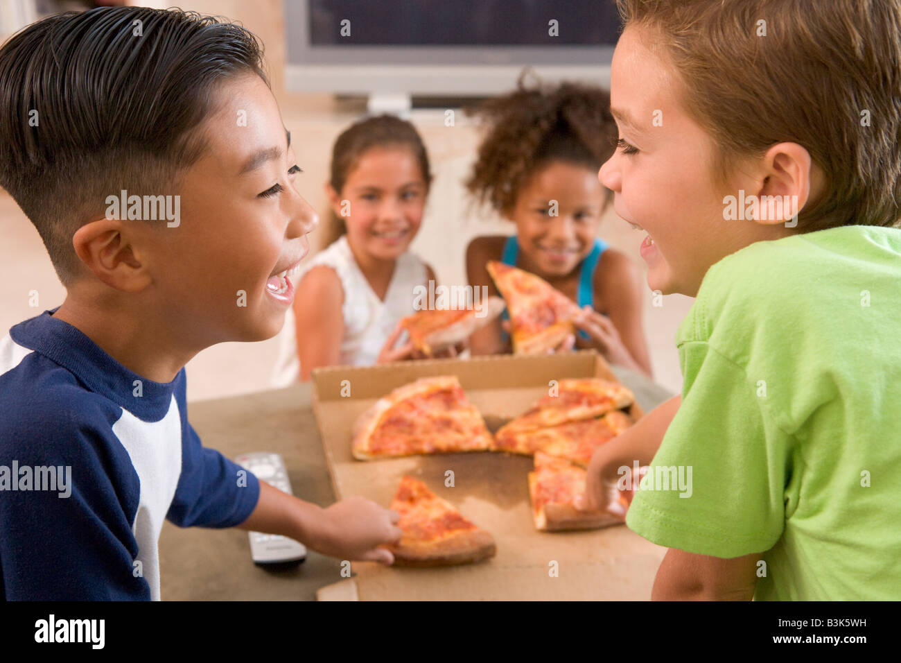 Quattro giovani bambini all'interno di mangiare pizza sorridente Foto Stock