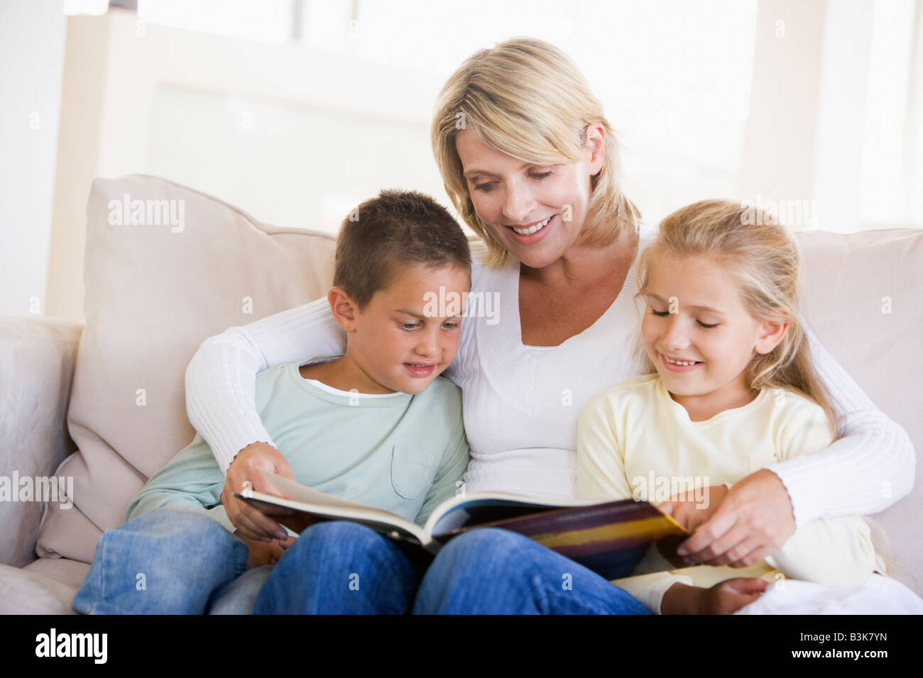 Donna e due bambini seduti nella sala lettura prenota e sorridente Foto Stock