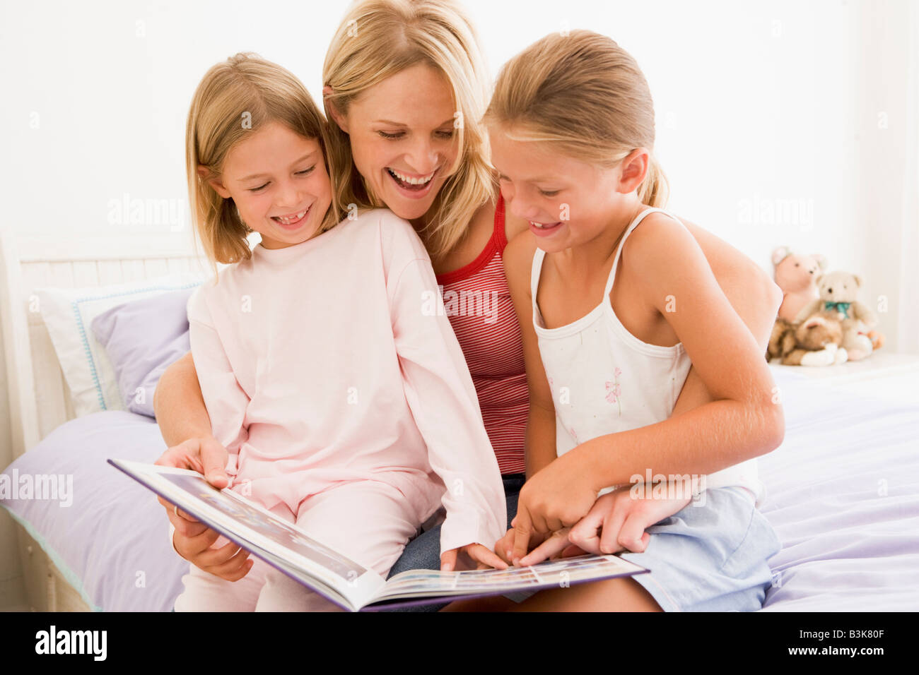 Donna e due giovani ragazze in camera da letto libri di lettura e sorridente Foto Stock