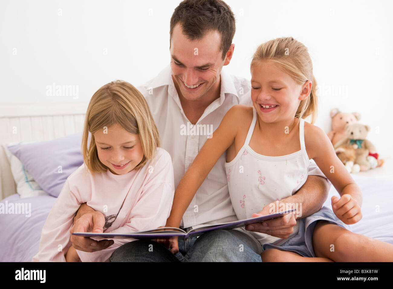 Uomo in camera da letto con due giovani ragazze libro di lettura e sorridente Foto Stock