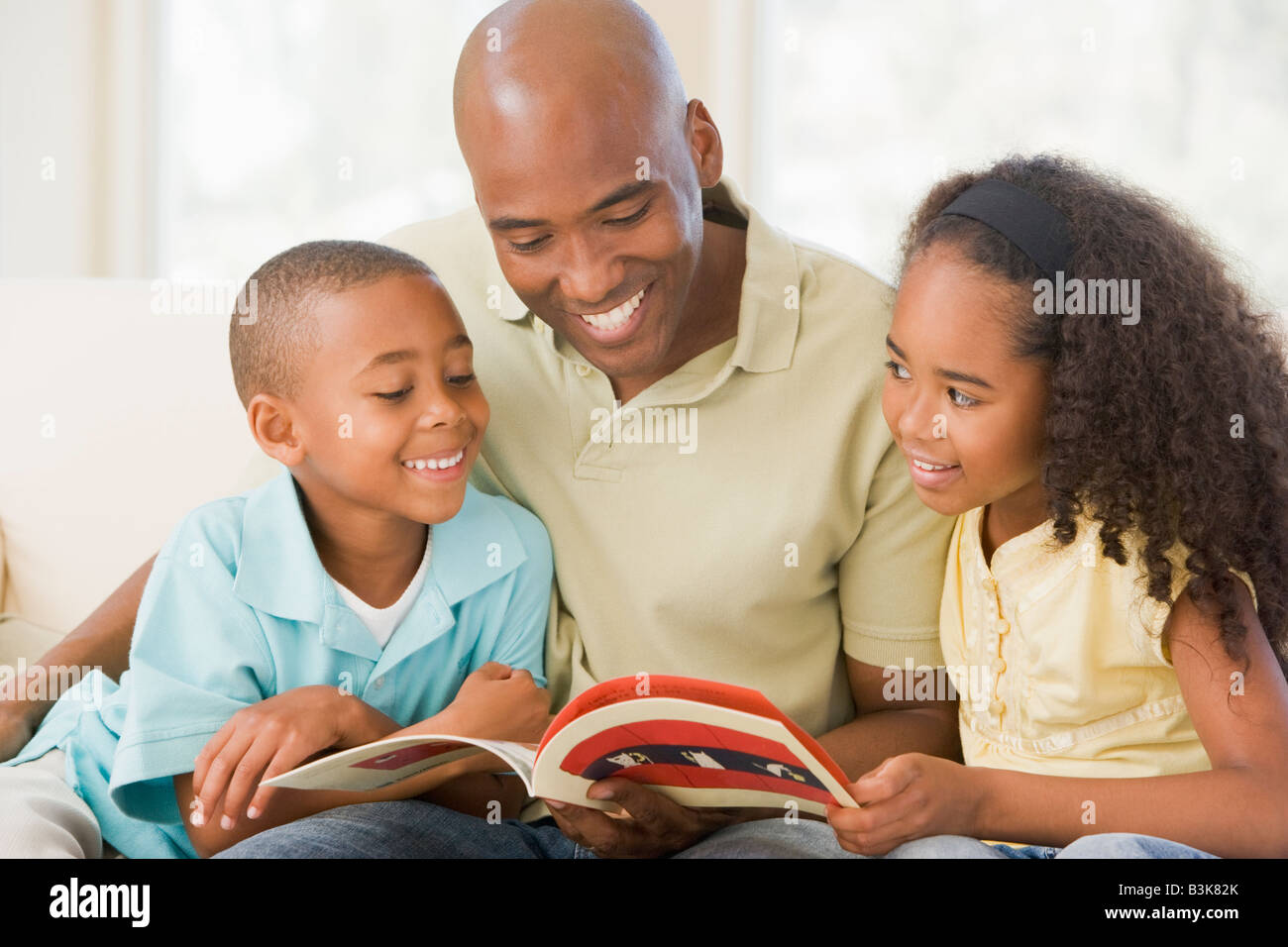 Uomo e due bambini seduti nella sala lettura prenota e sorridente Foto Stock