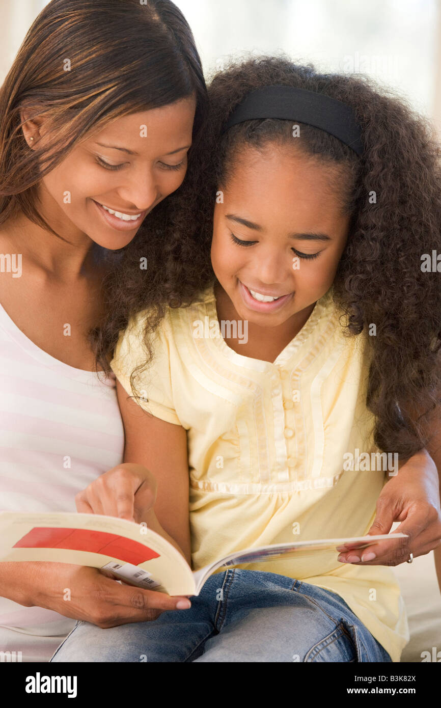 Donna e bambina seduta nel salotto lettura prenota e sorridente Foto Stock