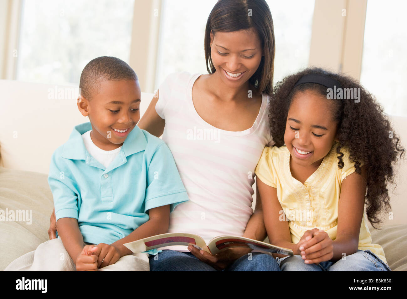 Donna e due bambini seduti nella sala lettura prenota e sorridente Foto Stock