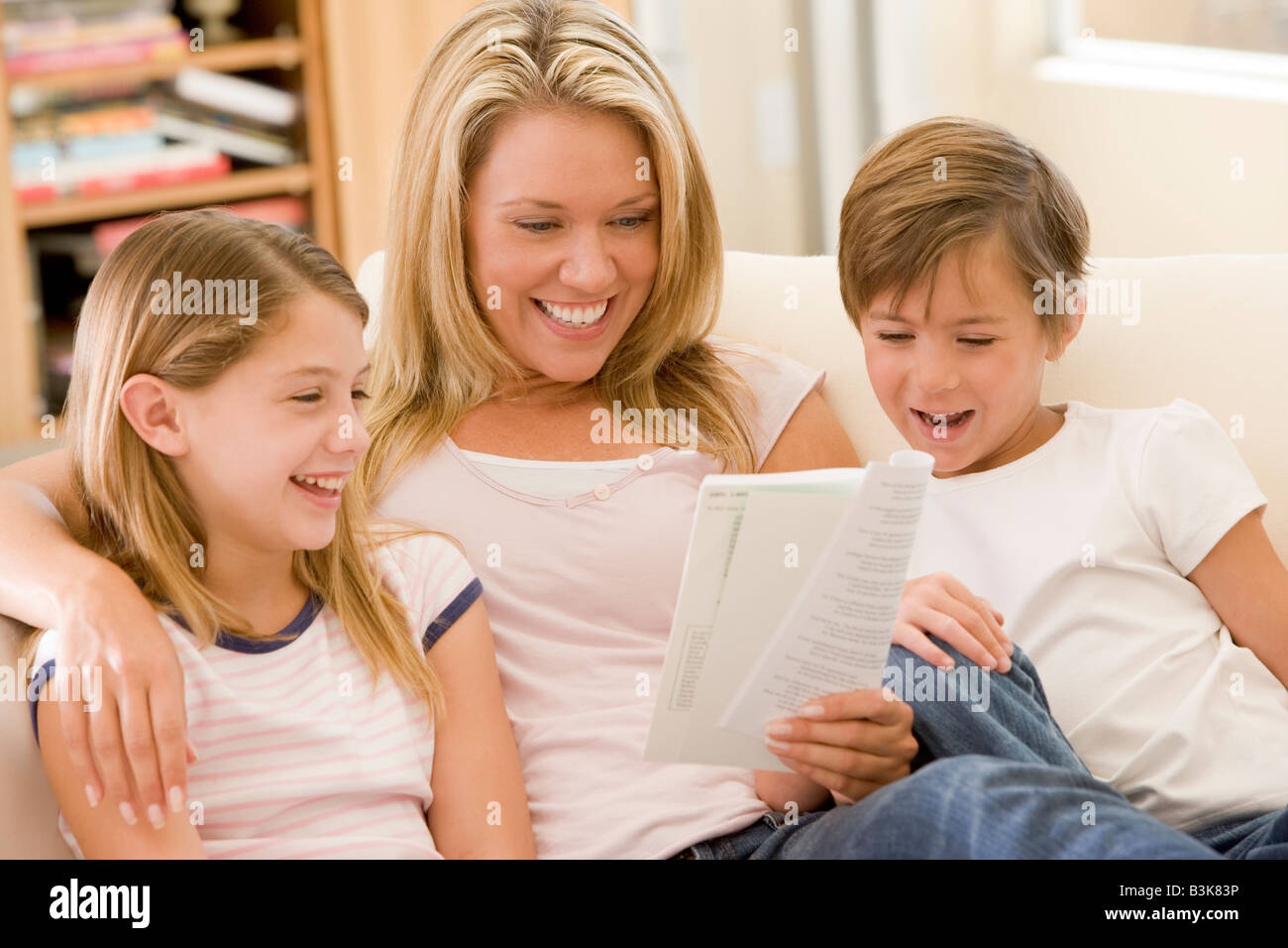 Donna e due bambini piccoli in sala lettura prenota e sorridente Foto Stock