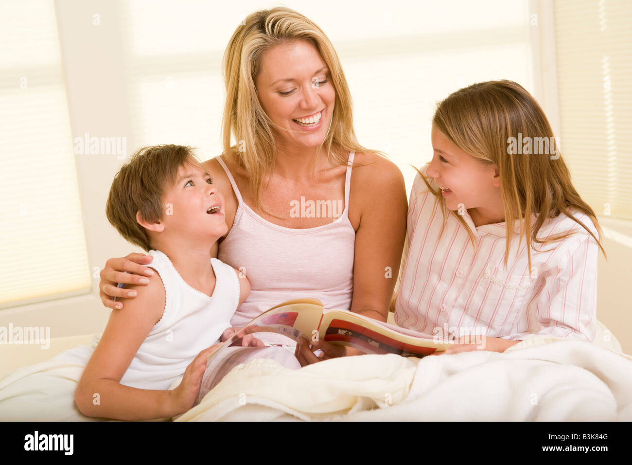 Donna con due giovani bambini seduti nel letto libri di lettura e sorridente Foto Stock