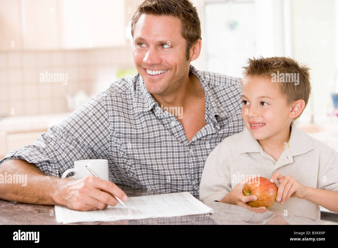 L uomo e il giovane ragazzo in cucina con apple di giornale e caffè sorridente Foto Stock