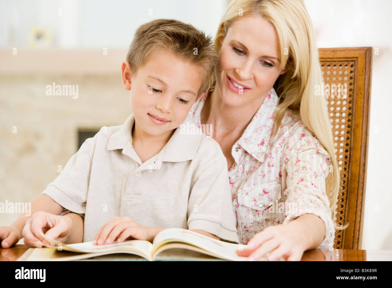 Donna e giovane ragazzo lettura libro in sala da pranzo sorridente Foto Stock