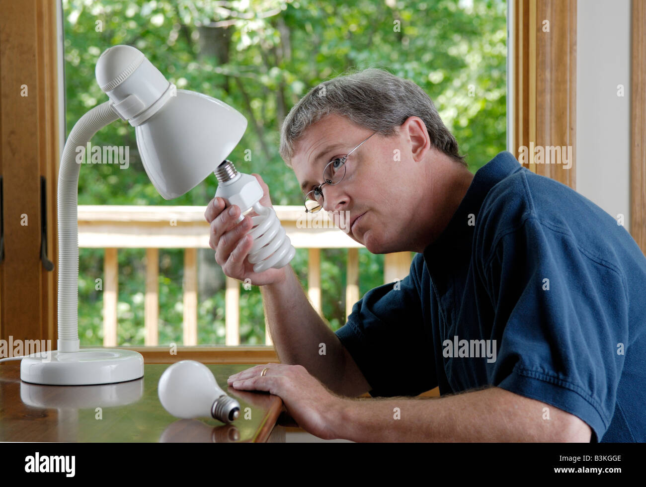 Un uomo di 45 anni sostituisce una famiglia di lampadine ad incandescenza con un risparmio energetico lampada compatta a fluorescenza Foto Stock