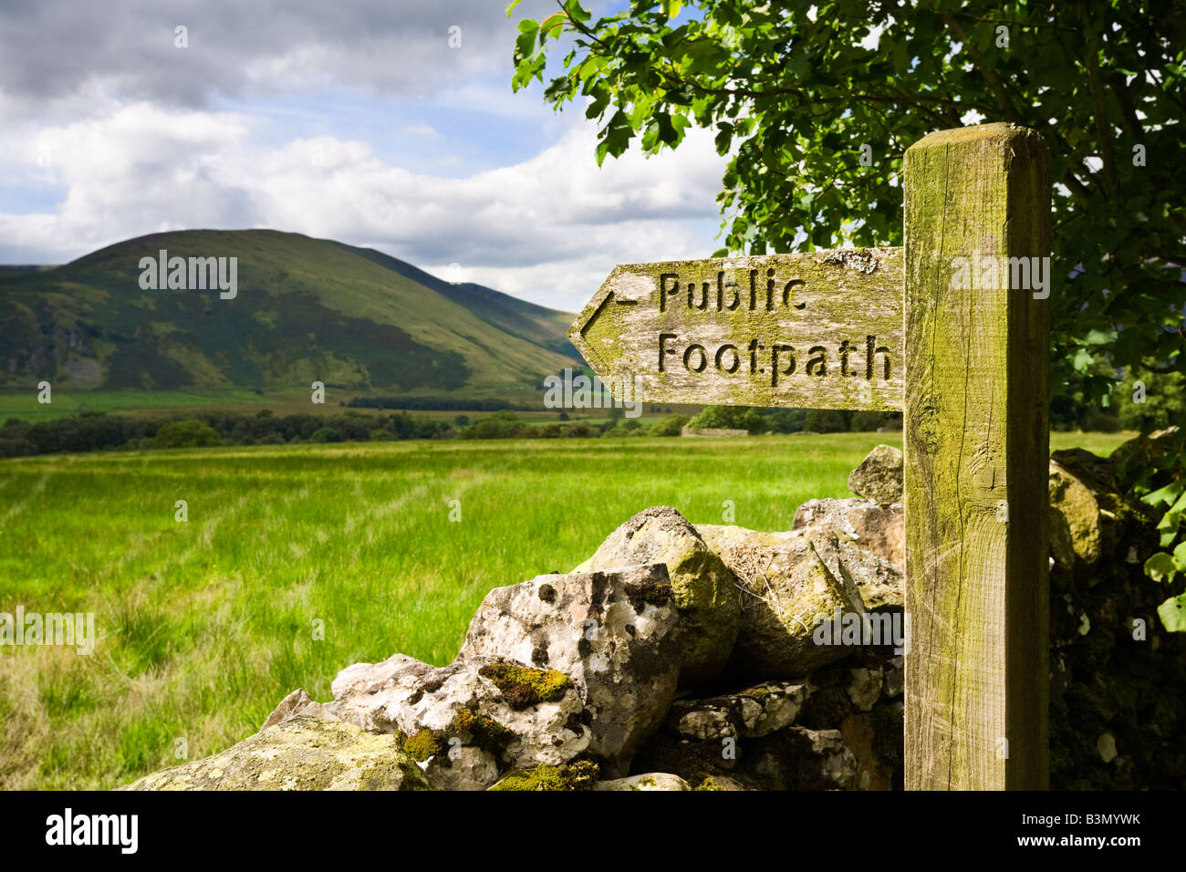 Di legno sentiero pubblico segno di orientamento e secco muro di pietra che si affaccia sul Lago di Rione Monti in Cumbria, England, Regno Unito Foto Stock