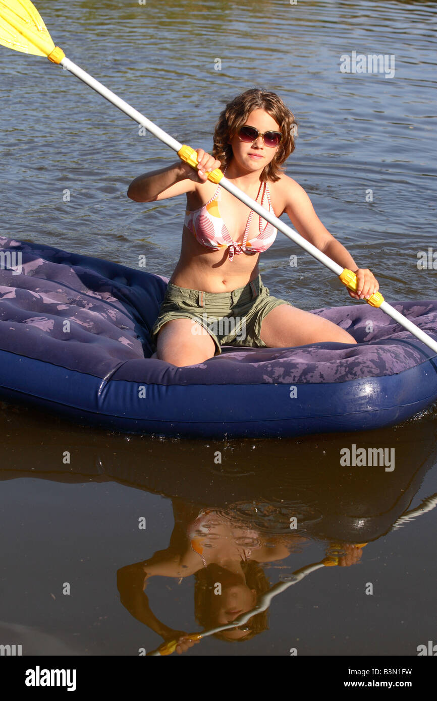 Ragazza adolescente su una zattera gonfiabile paddling attraverso un piccolo lago nella serata estiva Foto Stock