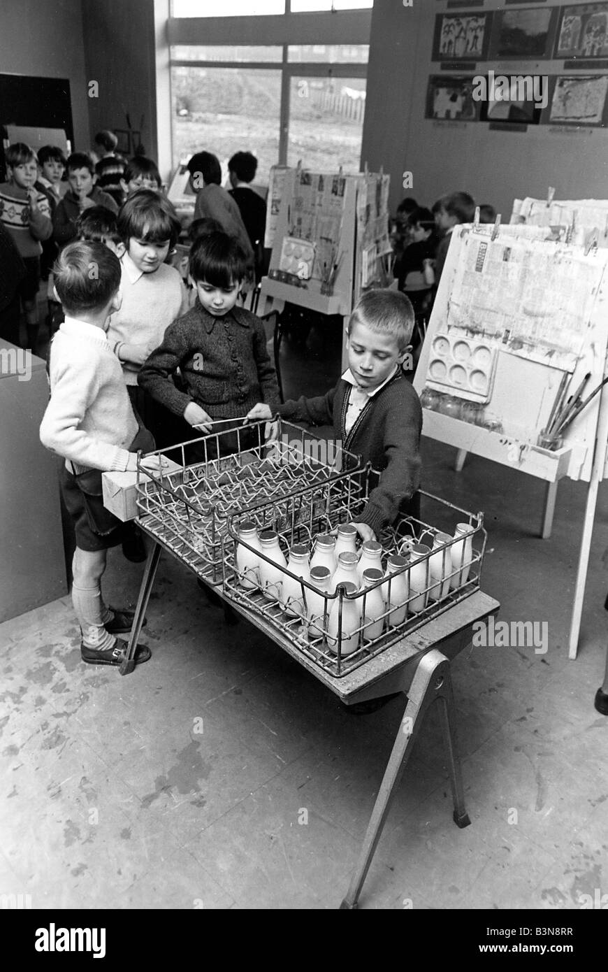 Tempo di latte latte mani monitor fuori la giornata è fornito ai compagni di alunni di una scuola del Regno Unito negli anni cinquanta a Foto Stock