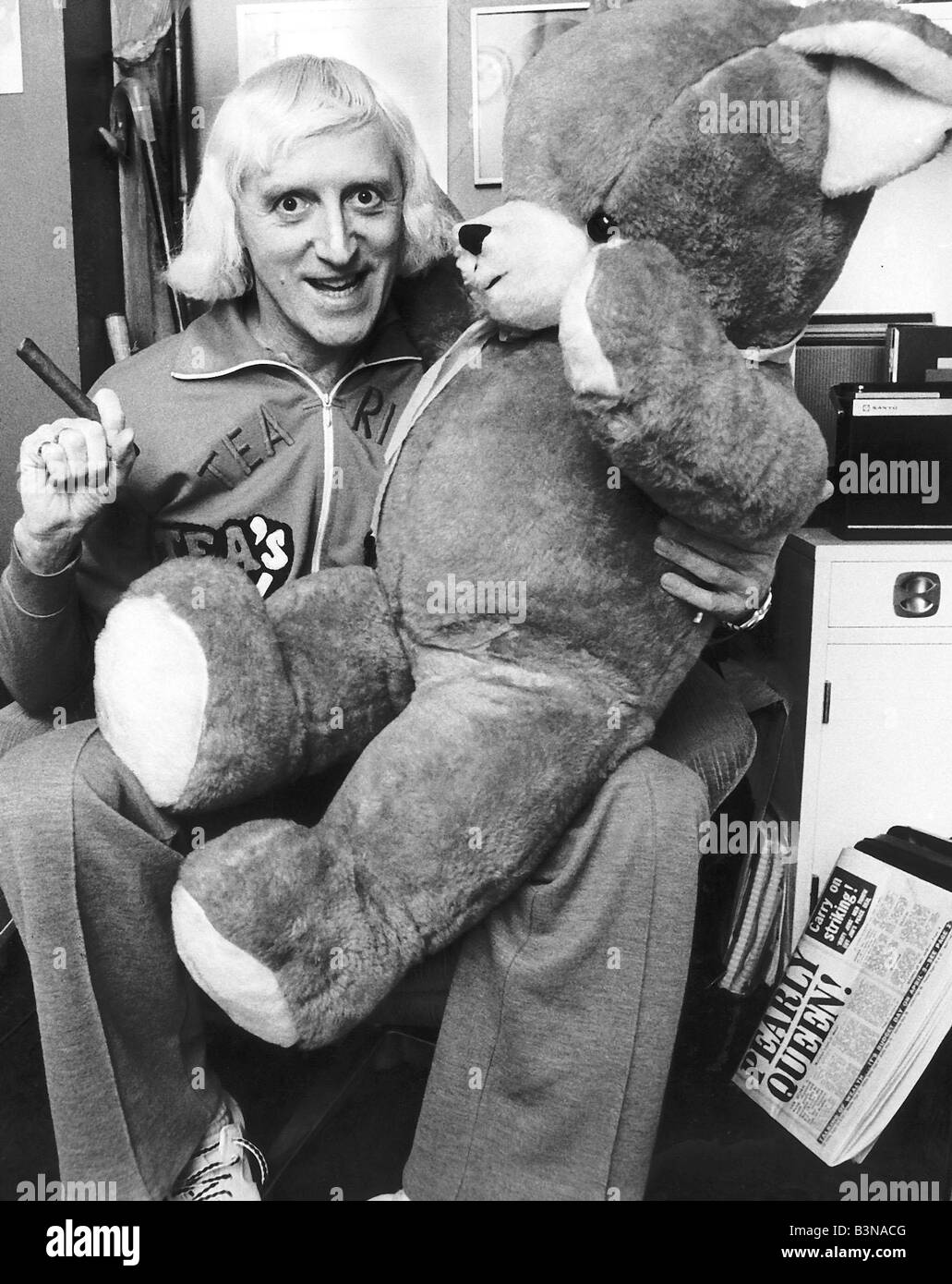Jimmy Saville DJ presentatore TV seduto in poltrona tenendo il sigaro e grande orso di peluche Foto Stock